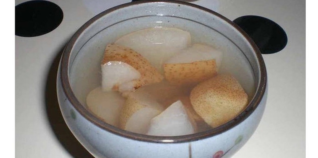 一碗热腾腾的川北雪梨炖品,梨子去核后填入少量川贝粉和冰糖,慢火炖至果肉透明软糯,汤色清澈微黄,盛放在白色瓷碗中,旁边点缀两朵干菊花,体现药膳养生氛围 川北雪梨炖川贝冰糖汤成品图