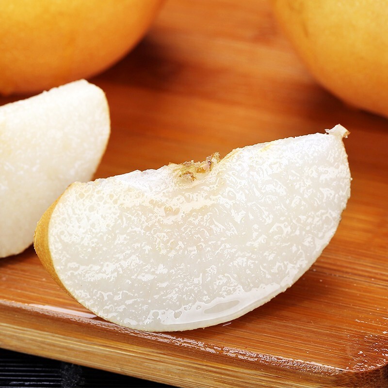 一个新鲜切开的早酥梨,果肉洁白细腻,质地紧实,汁水丰富,切面反射光泽,旁边放置一把不锈钢水果刀,背景为木质砧板和几片散落的梨片 早酥梨切面特写图