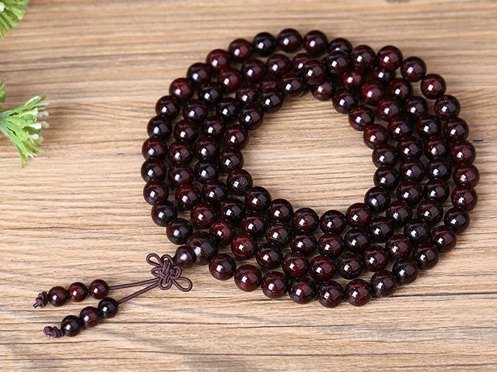 一串打磨光滑的小叶紫檀佛珠手链置于红木托盘上,旁边摆放一件小型紫檀雕刻貔貅摆件,背景为中式书房环境,突出其高端工艺与收藏属性 小叶紫檀制成的手串与雕刻摆件展示