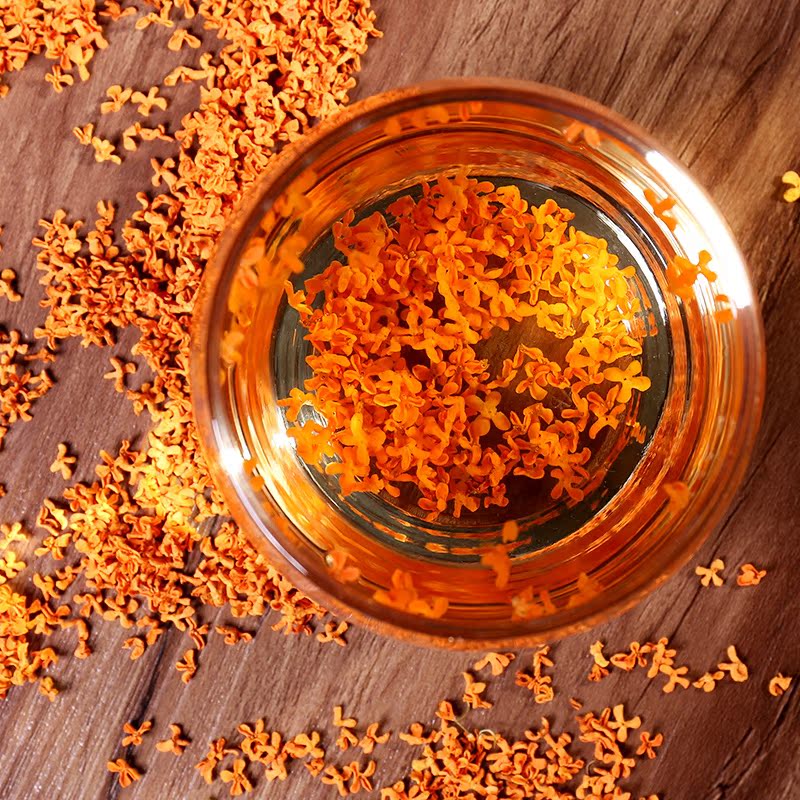 一张木质展台上陈列着多种以‘金桂飘香’为原料的深加工产品:玻璃瓶装桂花蜜、小罐冻干桂花、桂花香薰蜡烛、桂花茶包、桂花精油滴管瓶,背景为现代化农产品加工厂内景,光线柔和,突出产品的自然与高端质感 季桂深加工产品展示台