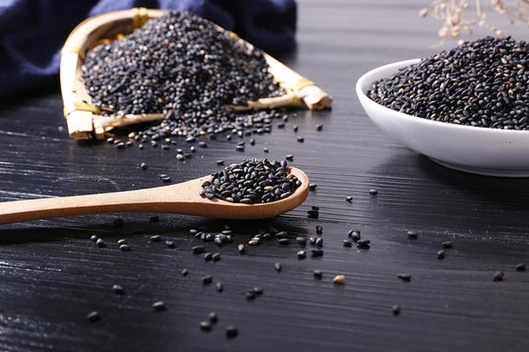 一张展示黑芝麻多种食用方式的拼图:左侧为炒香的黑芝麻粒,中间为研磨后的黑芝麻粉,右侧为加入燕麦粥和酸奶杯中的应用场景,旁边配有铜勺和玻璃罐,体现日常养生饮食场景 黑芝麻食品搭配示意图