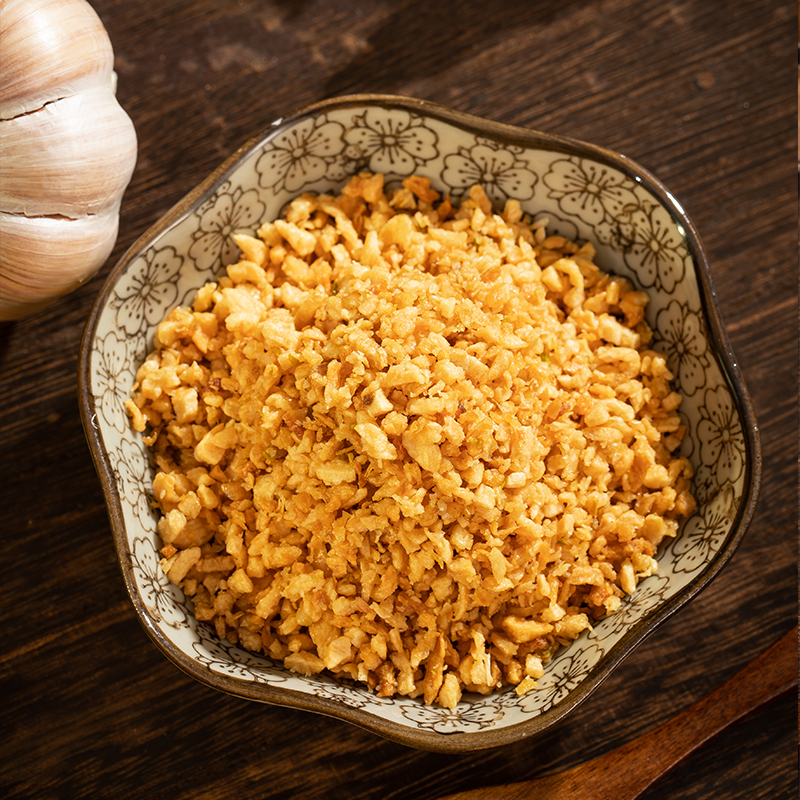 一道正在烹饪中的菜肴,锅中为金黄色蒜香鸡块,表面覆盖着细碎的独头蒜末,油光闪亮,蒸汽袅袅上升。旁边摆放未使用的完整独头蒜和压蒜器,体现食材到成品的过程。拍摄角度为俯视45度,背景为现代中式厨房环境 独头蒜入菜烹饪过程图