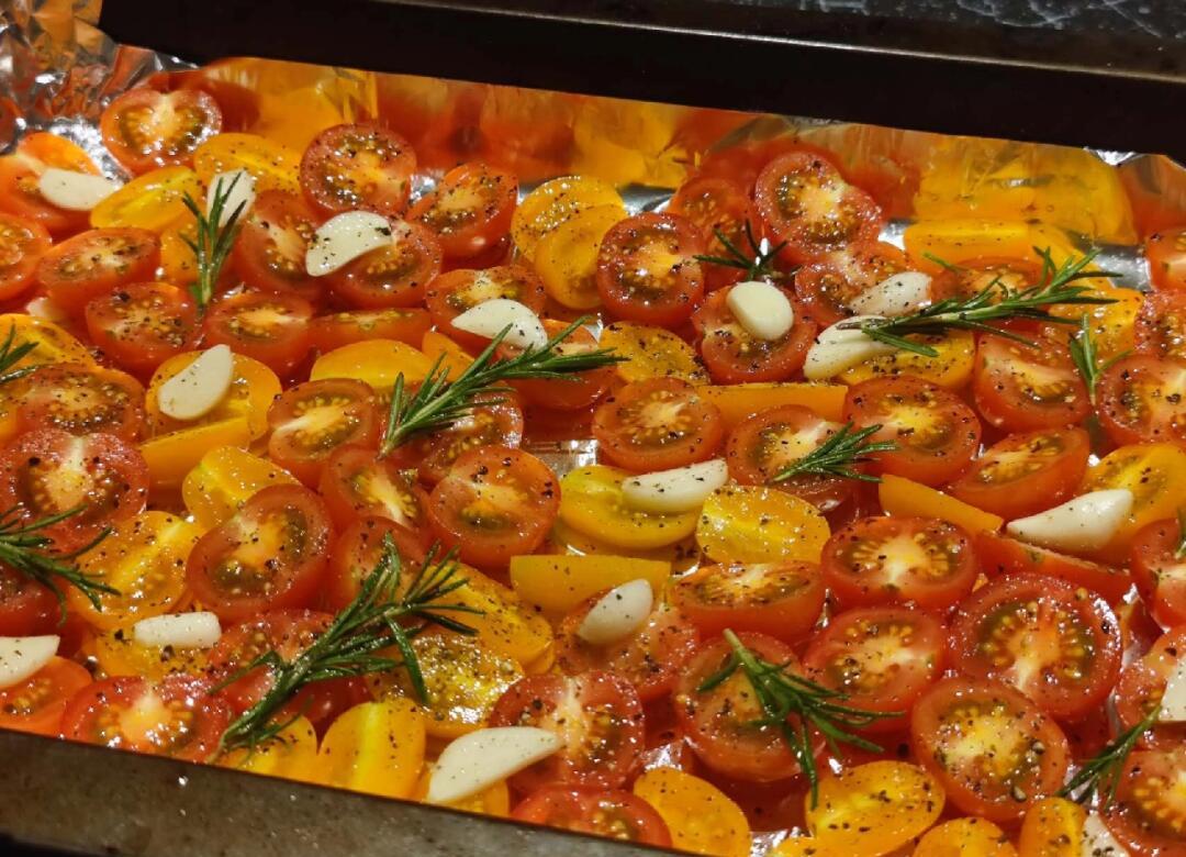 烤盘中排列整齐的半颗普罗旺斯番茄，切面朝上，表面泛着油光，撒有香料，正在烤箱中慢烤