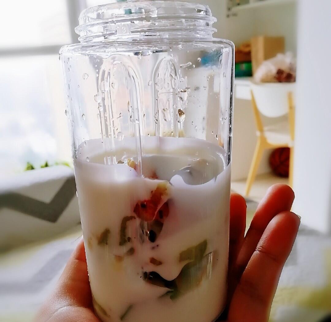 一杯盛满乳白色奶昔的玻璃杯，旁边放着半根香蕉和一小碟切好的海参丁