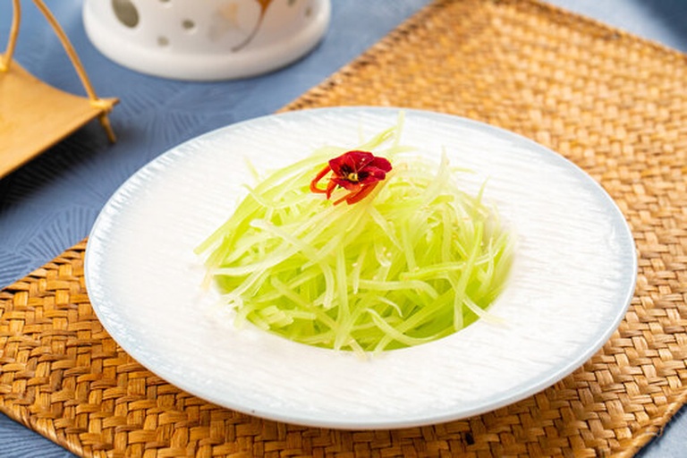 一盘精致的凉拌莴苣丝盛放在浅色陶瓷盘中,莴苣丝洁白纤细,表面点缀着金黄的烤芝麻、红色的小米辣圈和翠绿的葱花,旁边摆放一双竹筷,背景为简约餐桌布景 凉拌莴苣丝成品展示