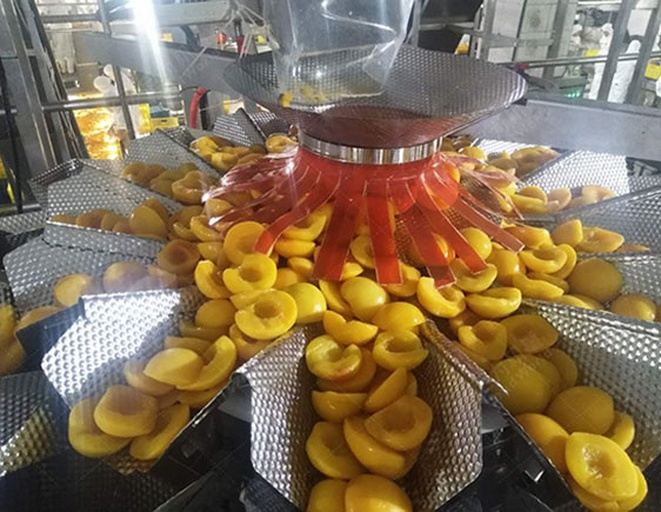 桃熏产后处理场景,展示标准化分拣与品牌化包装流程 打包车间内工人正在分拣桃熏果实,按大小分级放置于环保纸托中,背景有品牌标识和冷链运输箱