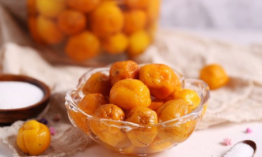 一位农民在乡村庭院中手工制作金桔蜜饯,桌上摆放着洗净的金桔、玻璃罐、冰糖和不锈钢锅,锅中金桔正在慢火熬煮,蒸汽袅袅升起,体现传统农产加工工艺的真实场景 金桔加工场景图