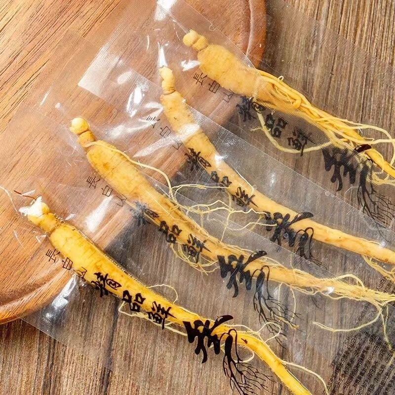 一位中年女性在正规药店柜台前咨询药师,手中拿着一盒标注‘长白山5年生鲜人参’的透明包装产品,背景陈列着其他中药材,体现专业选购环境 消费者选购鲜人参场景