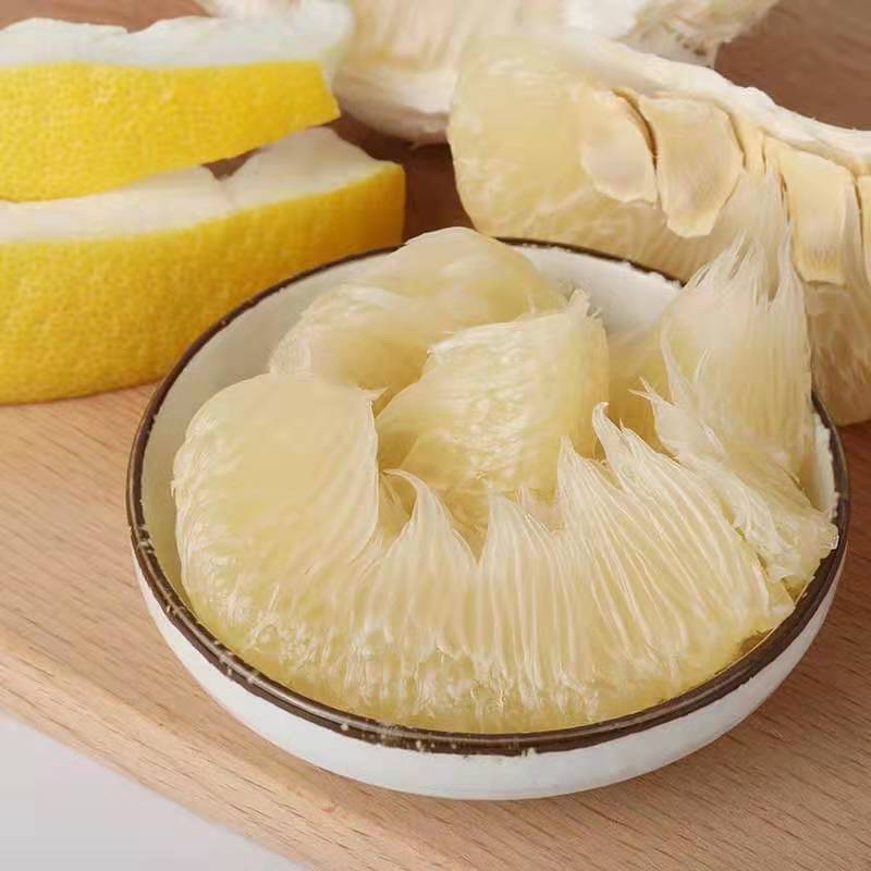 一位厨师正在白色桌面上用手指和小剪刀仔细剥离柚子果肉的透明薄膜,旁边放着一碗已处理好的粉红色柚子果粒,背景为厨房环境,光线柔和自然 柚子果肉手工剥离过程