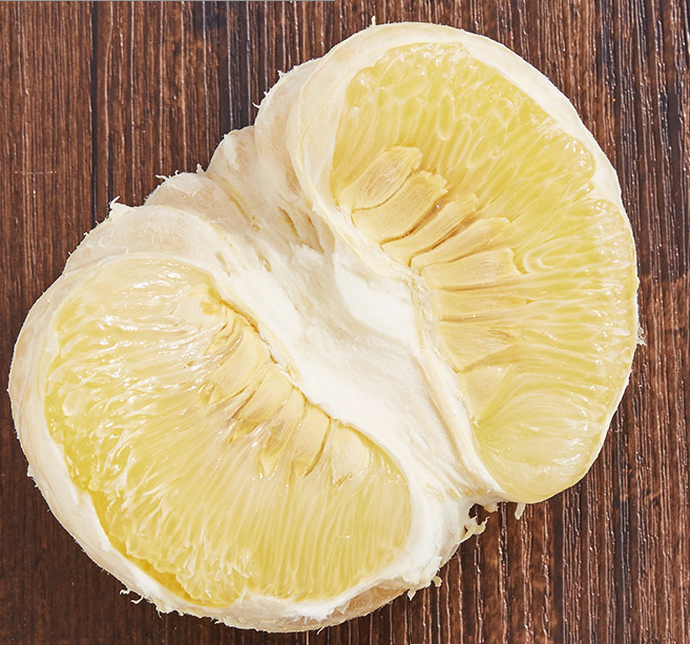 一个新鲜的柚子被横向切开,露出饱满水润的淡黄色果肉,汁水清晰可见,周围有几片剥好的果瓣摆放在木质餐盘上,背景为柔和自然光下的厨房环境 柚子切开特写