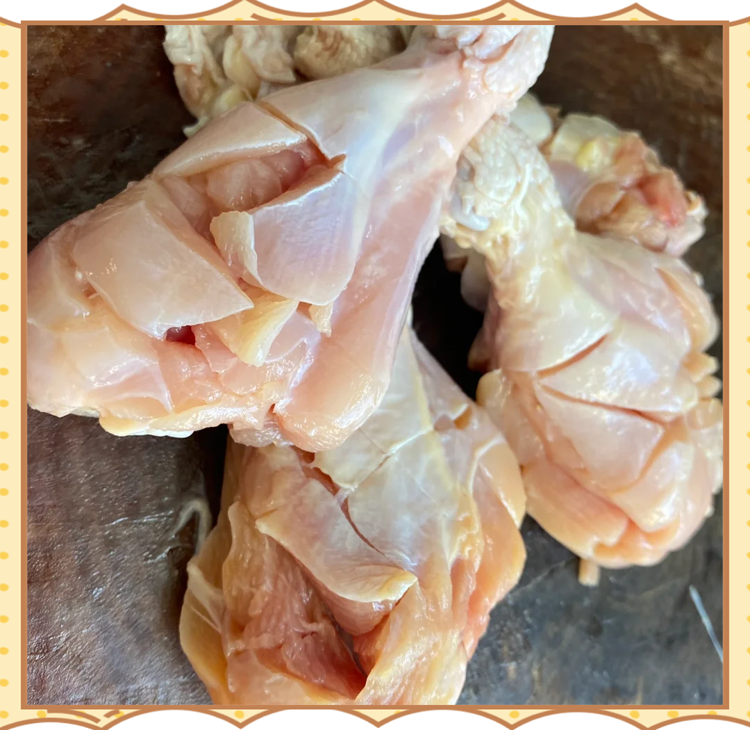 一只新鲜带皮鸡腿平放在木质砧板上,表皮呈淡黄色,肌肉纹理清晰可见,边缘略带红色血丝,背景为厨房环境,光线自然柔和 鸡腿特写