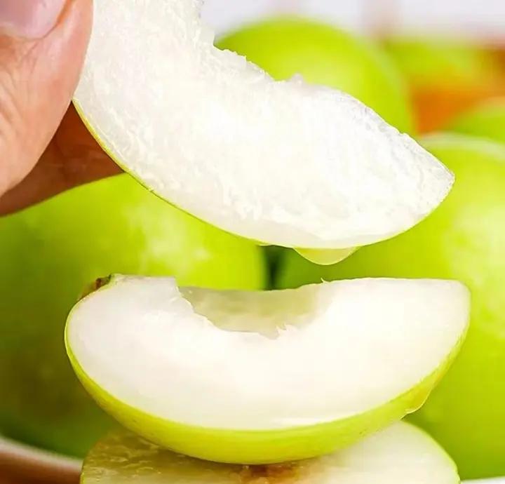 一张高清特写图展示三到五颗新鲜青枣,果皮呈翠绿色略带金黄晕染,表面光亮无损,旁边有一把白色陶瓷刀正在切开其中一颗,露出洁白多汁的果肉,背景为木质餐桌与玻璃水杯,营造出清新自然的家庭食用场景 青枣特写与食用场景