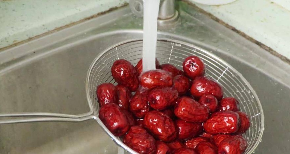 一位女性正在厨房用流动水清洗红枣,手中拿着几颗鲜红的红枣 清洗红枣的场景