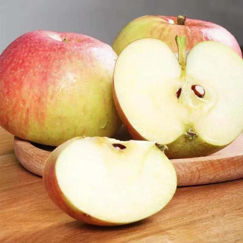 一盘切开的红将军苹果摆放在木质餐桌上，旁边配有蜂蜜和坚果