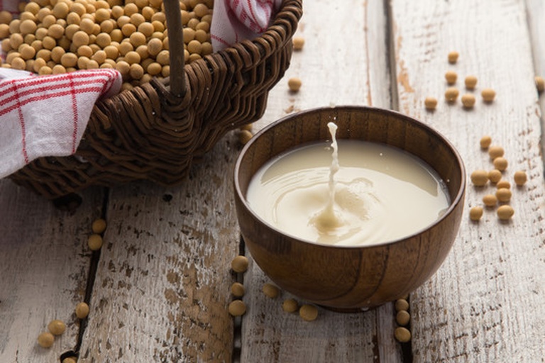 一杯刚打好的黑豆香蕉浆放置在白色陶瓷杯中,液体呈深棕色带轻微光泽,表面无明显泡沫,旁边配有搅拌勺和半根未使用的香蕉作为装饰,背景为厨房操作台,展现家庭制作场景 黑豆香蕉浆成品展示