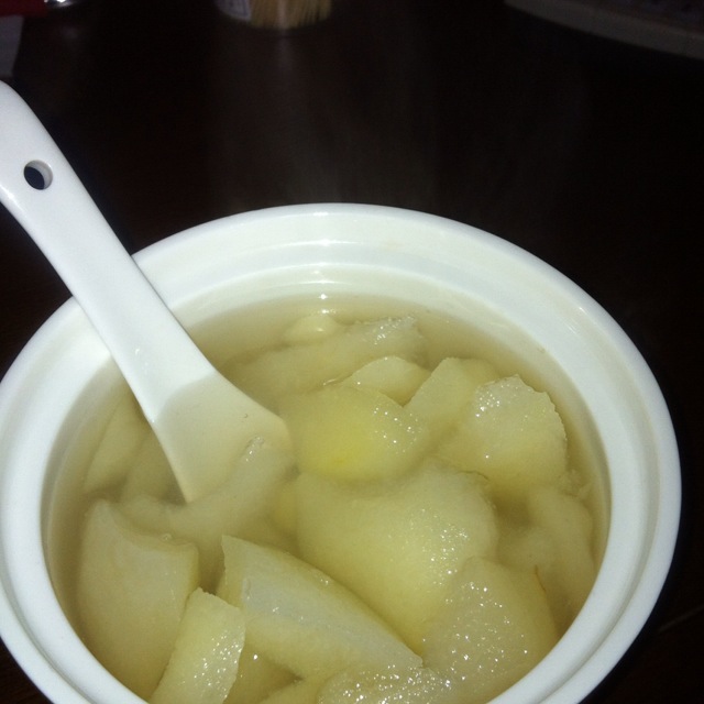 农贸市场冬季专区,木质货架上整齐码放着数十个表面覆盖薄霜的黑色冻酸梨子,旁边立有手写招牌‘正宗东北冻酸梨 润肺止咳’字样,顾客正在挑选购买,背景可见其他冬季特产如冻柿子、冻草莓等 市场摊位上整齐摆放的黑色冻酸梨子与宣传牌