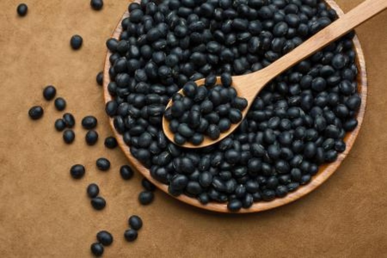 一只手正用木勺从电饭煲中盛出热气腾腾的黑豆杂粮饭,米饭中可见黑色豆粒均匀分布,色泽自然,旁边摆放竹筷和白色瓷碗,展现中式健康饮食场景 黑豆杂粮饭盛出过程