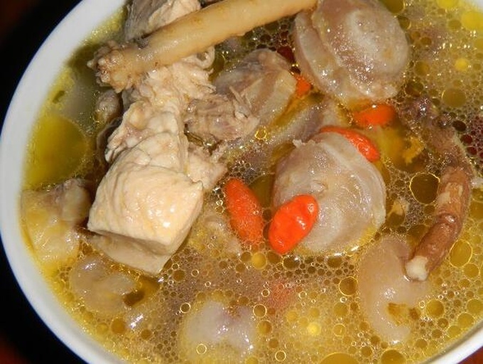 一碗热气腾腾的鹿鞭炖鸡汤,汤色金黄清澈,可见鹿鞭切片、枸杞、红枣和鸡肉块,旁边配有瓷勺和木制餐垫,背景为中式厨房环境 鹿鞭炖汤成品