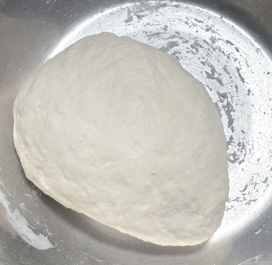 一台工业级立式和面机正在运转,不锈钢缸体内是正在揉捏的巨大白色面团,操作人员戴手套观察面团状态,背景为干净整洁的食品加工车间 百斤面团在大型和面机中揉制过程