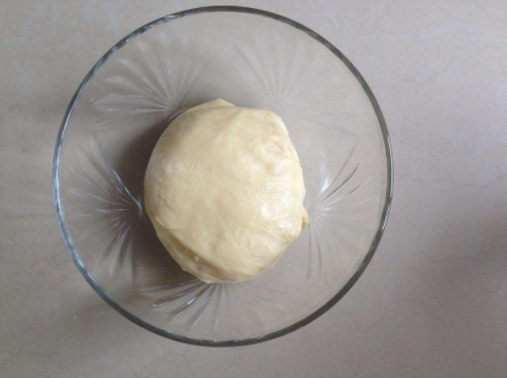 一名厨师正在用玻璃杯底部在金属派盘中压实消化饼干与融化的黄油混合物,台面上有散落的饼干碎和黄油瓶,背景为厨房操作台 巧克力派皮压制过程