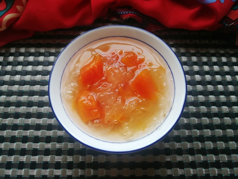 木瓜牛奶炖雪燕成品特写：白瓷深口碗中盛满温润琥珀色羹体，表面浮着几粒饱满木瓜丁，汤汁清澈透亮，勺子轻舀可见细腻拉丝与柔滑质地