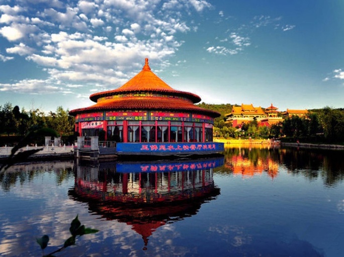 一座中式亭子旁种植着数棵五角枫,红叶掩映着飞檐翘角的屋顶,石板小径铺满落叶,一位游客撑伞缓步前行,整体画面充满古典意境与秋日诗意,背景为薄雾缭绕的湖面 五角枫与园林建筑融合景观