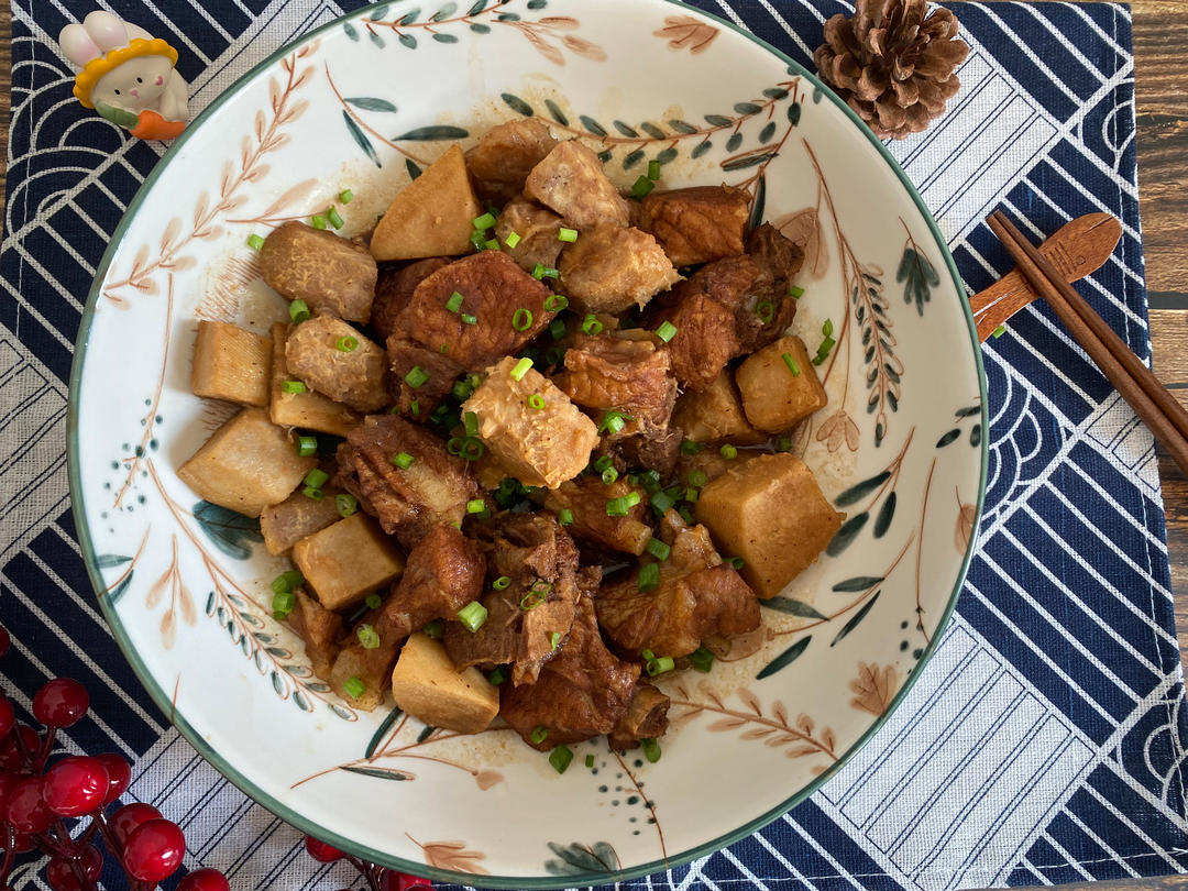 深色砂锅中盛着油亮诱人的红烧芋头与排骨,汤汁浓郁,周围点缀葱花,背景为中式餐桌 一盘热气腾腾的红烧芋头排骨