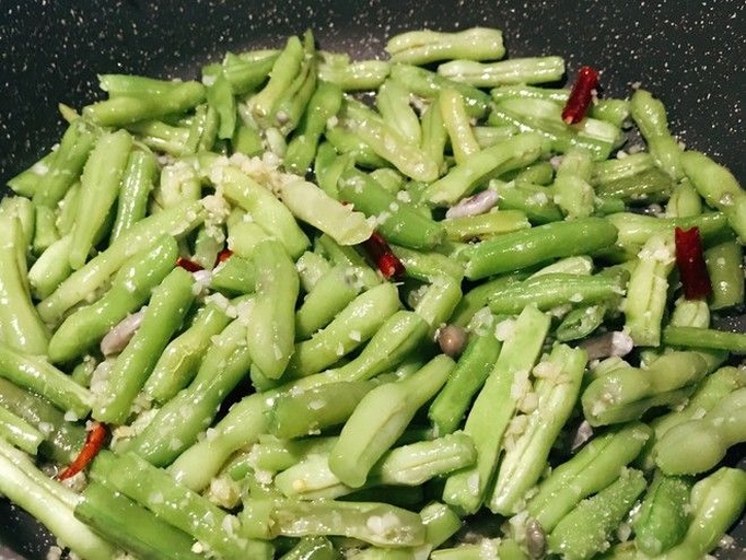 炒锅中正在翻炒的短豆角与土豆混合食材,颜色呈金黄与翠绿交织,锅气升腾,蒜片清晰可见,体现旺火快炒的真实场景 短豆角和土豆翻炒过程