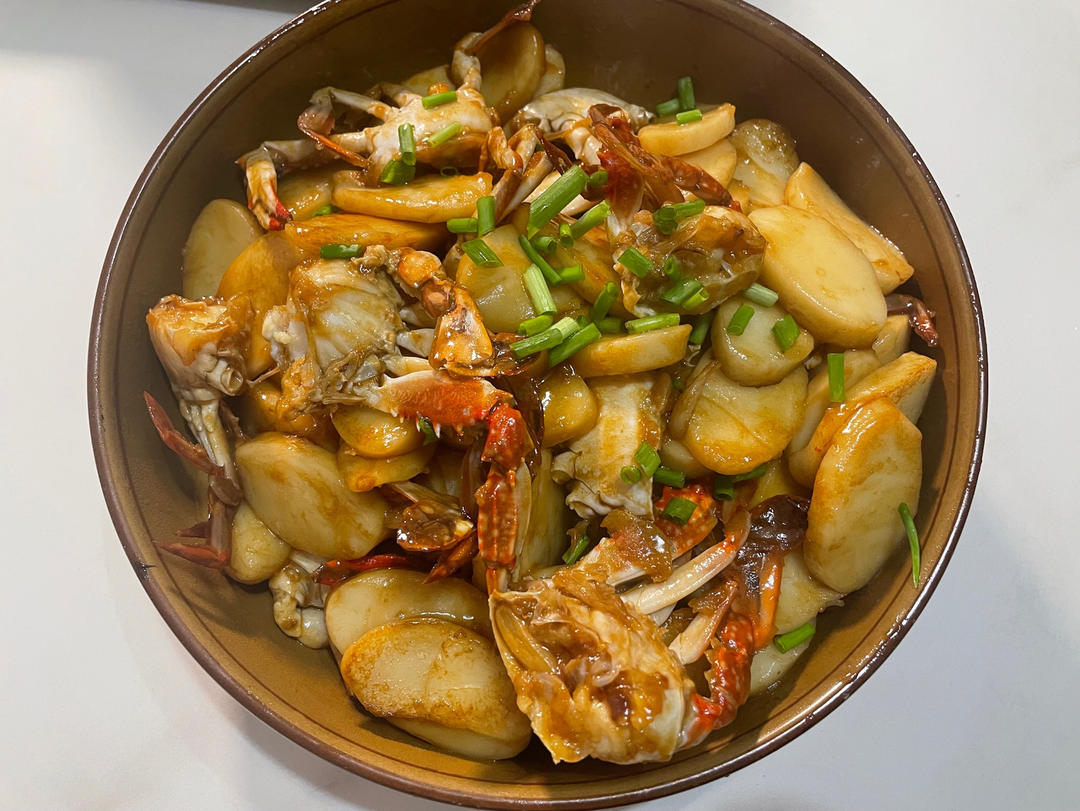 铸铁锅中正在炖煮的年糕梭子蟹,橙红色的蟹块与乳白色年糕交织,汤汁浓稠适中,表面泛着油光,锅边可见姜片与葱段,热气蒸腾 年糕与梭子蟹在锅中炖煮过程