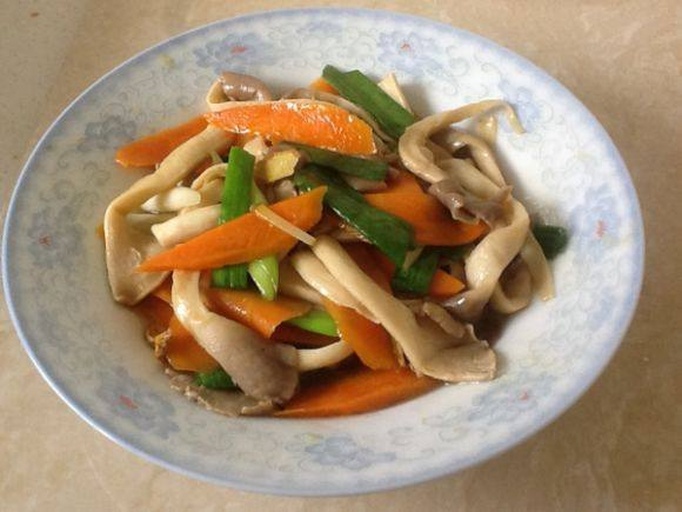 平菇炒胡萝卜成品展示 一盘刚出锅的平菇炒胡萝卜,胡萝卜片呈半透明橙红色,平菇洁白柔润,整体略带酱汁光泽,盛放在白色瓷盘中,背景为木质餐桌