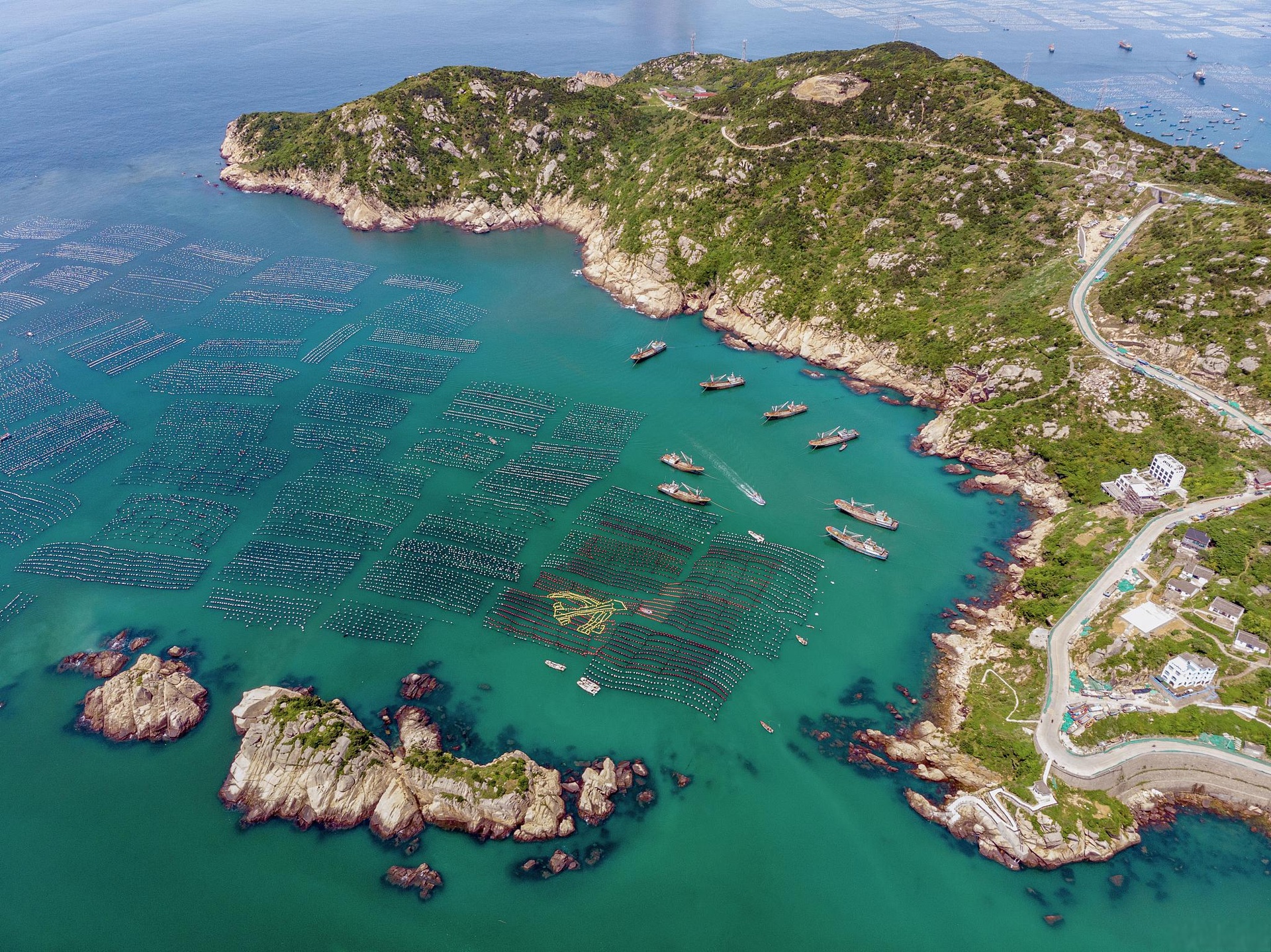 浙江省台州市三门县三门湾海域全景航拍图,展示蜿蜒海岸线、滩涂湿地与近海渔排分布,海水呈蓝绿色,可见渔船作业场景,背景为连绵丘陵地貌 三门湾海域航拍图