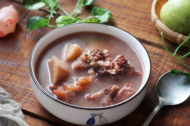 一碗温热的四物汤置于木桌上,汤色呈琥珀色,表面略有油光,旁边配有陶瓷勺和一杯清水,背景虚化显示中式厨房环境,传递温暖养生的生活方式氛围 四物汤成品与饮用场景