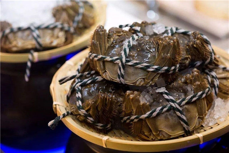 一个清晨的水产市场摊位,多个透明塑料筐中装有活蹦乱跳的大闸蟹,摊主正在捆扎蟹钳,顾客在挑选,背景可见‘阳澄湖大闸蟹’招牌和电子秤,展现真实采购场景 大闸蟹市场选购场景
