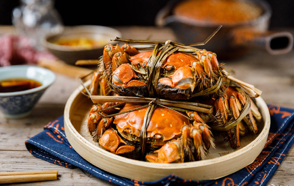 一张中式餐桌上的清蒸大闸蟹特写,三只完整的大闸蟹整齐摆放在白瓷盘中,蟹壳橙红油亮,旁边配有小碟姜醋汁、紫砂壶和筷子,营造出秋季品蟹的温馨氛围 家庭餐桌上摆放着清蒸大闸蟹的场景