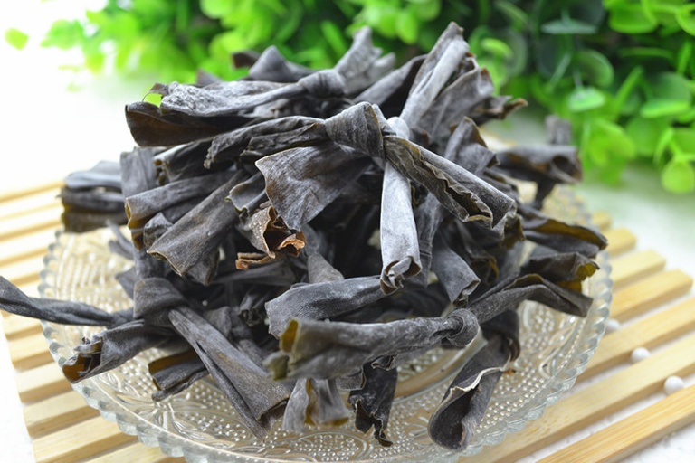 一个透明玻璃密封罐中装有干燥的深褐色条状干海带,罐口紧闭,旁边放置一包小型食品级硅胶干燥剂,背景为厨房储物柜内部,光线柔和,体现阴凉干燥的储存环境 干海带密封保存示意图