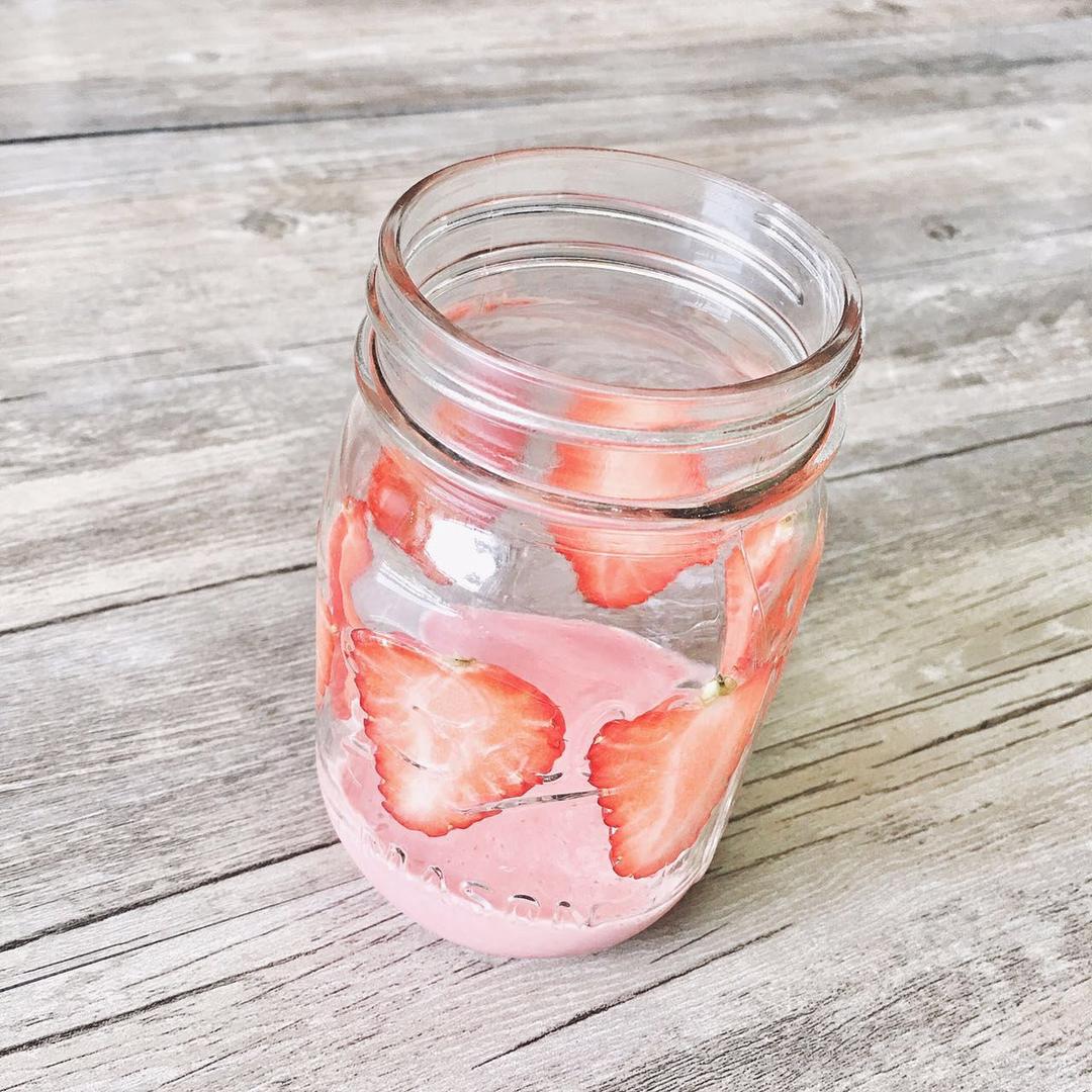 玻璃碗中盛放着淡粉色的自制苹果酸奶沙拉酱，旁边摆放着苹果块、酸奶罐和调料瓶，桌面为木质背景