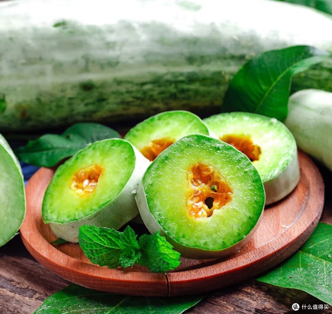 一个刚切开的新鲜哈密瓜放置在厨房台面上,左侧有一卷保鲜膜,背景隐约可见冰箱门打开,光线明亮,营造出家庭厨房的真实场景 切开的哈密瓜放在白色瓷盘中,旁边有保鲜膜和冰箱背景