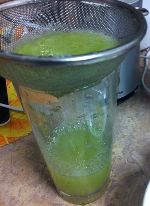 操作台上摆放着榨汁机、玻璃量杯、滤网、青提果粒和刚榨出的淡绿色果汁,一名厨师正在用滤网过滤果汁,桌面整洁,光线柔和,展现家庭自制青提汁的真实场景 青提榨汁过程实拍图