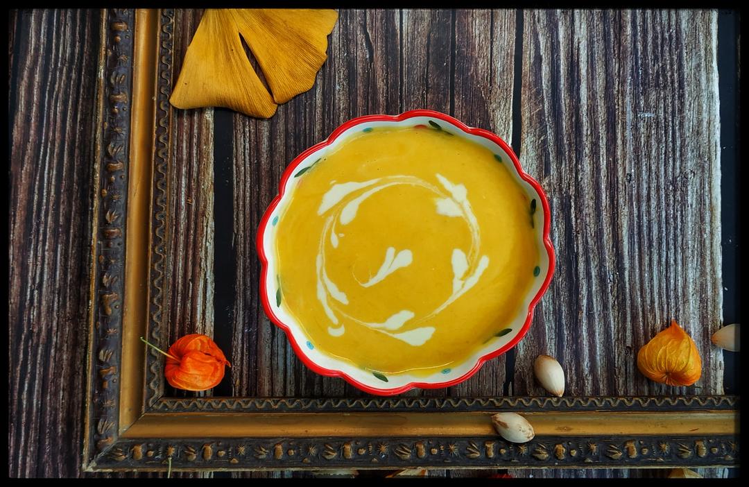 成品摆盘特写：纯白陶瓷浅碗盛装琥珀色奶油南瓜浓汤，表面淋一圈金棕色乳脂奶油，撒现磨黑胡椒与烤南瓜籽，汤面倒映柔和光影，背景虚化为暖调砖墙与绿植