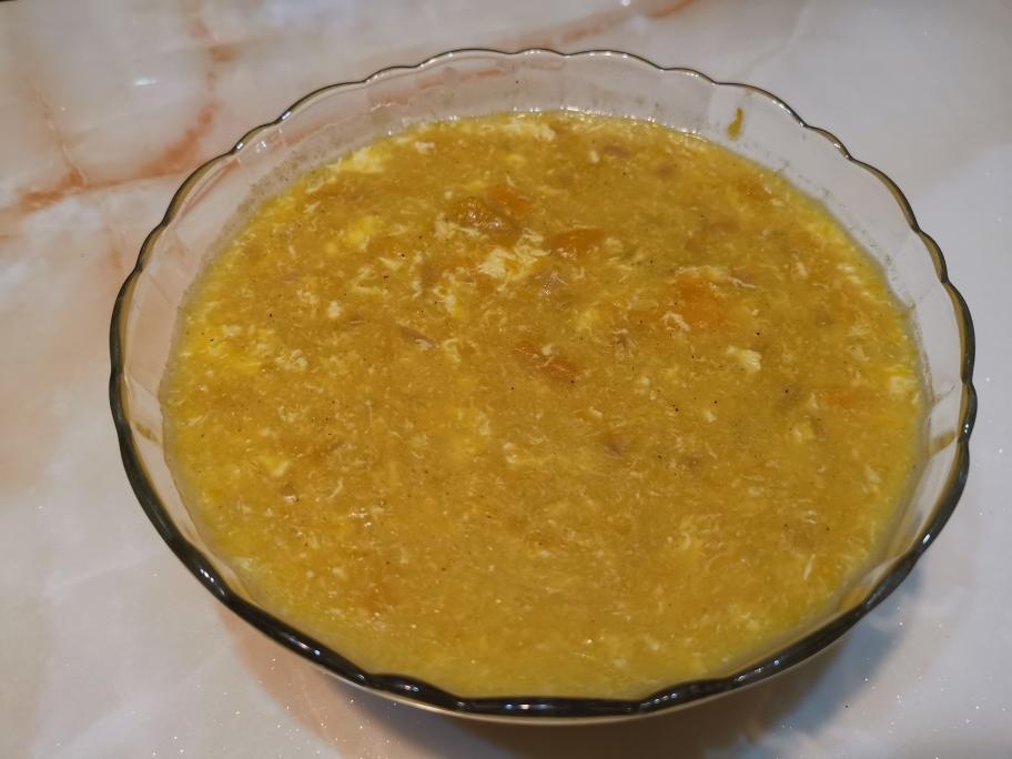 金黄色的南瓜豆浆倒入玻璃杯中，旁边放着南瓜块和黄豆