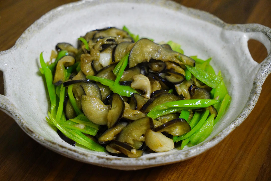 一盘装好的地三鲜摆放在白色瓷盘中,茄子呈深褐色、土豆金黄、青椒翠绿,整体色泽油亮诱人,旁边配有米饭和竹筷 图片描述