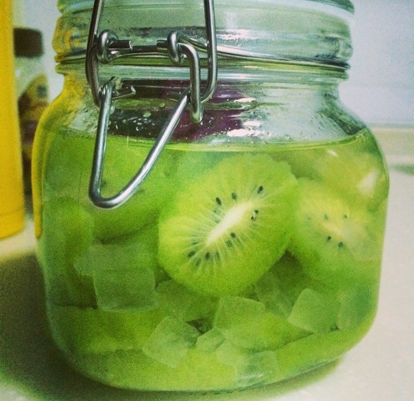 透明玻璃发酵罐装有正在冒泡的淡黄色猕猴桃酒液，连接着橡胶塞和水封阀