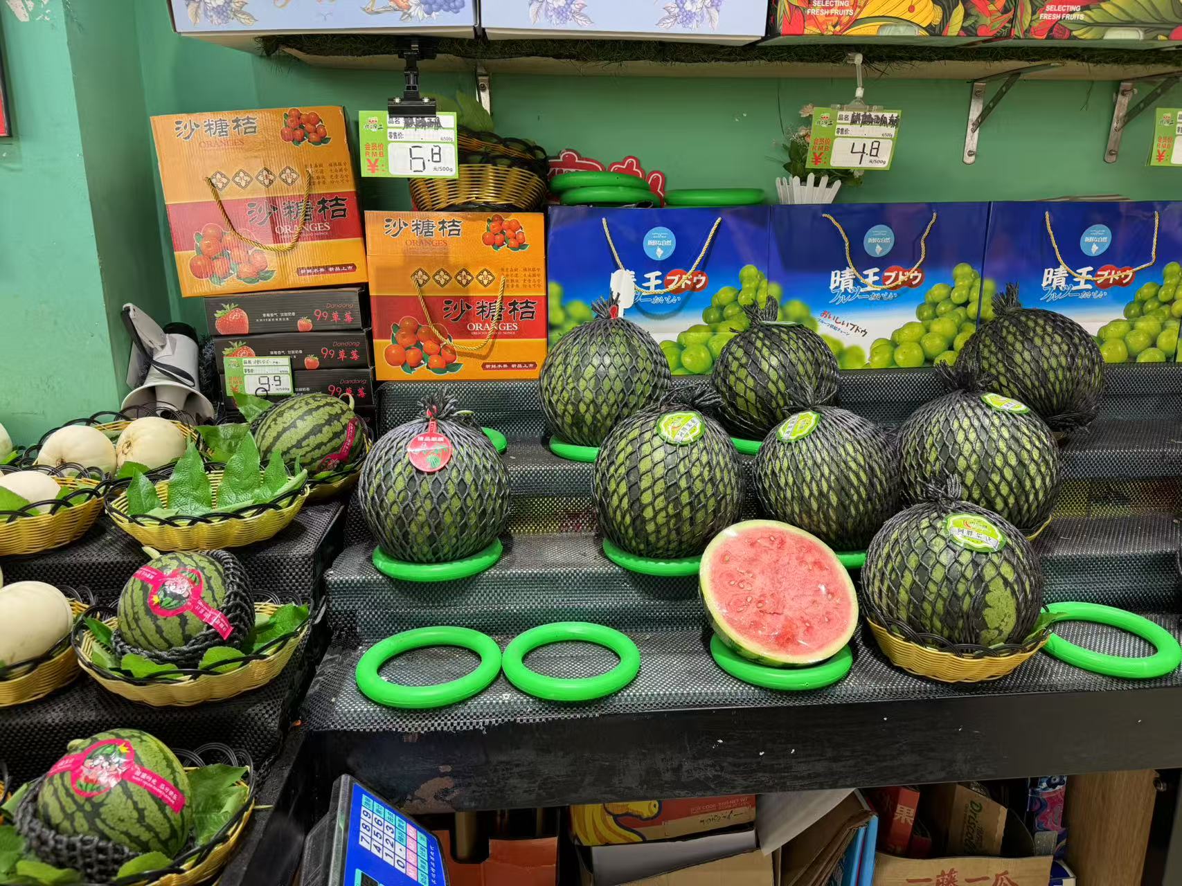 现代超市水果货架上整齐摆放着不同种类的西瓜,包括深绿条纹红瓤西瓜、浅绿皮黄瓤西瓜以及小型圆形西瓜,标签上标注价格和品种名称,顾客正在挑选 超市水果区陈列的多种西瓜