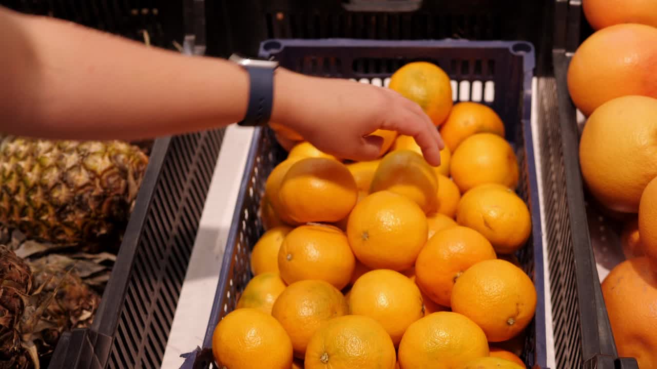 一位消费者正在超市挑选橙子,仔细观察橙子底部的凹陷与凸起 橙子的挑选场景