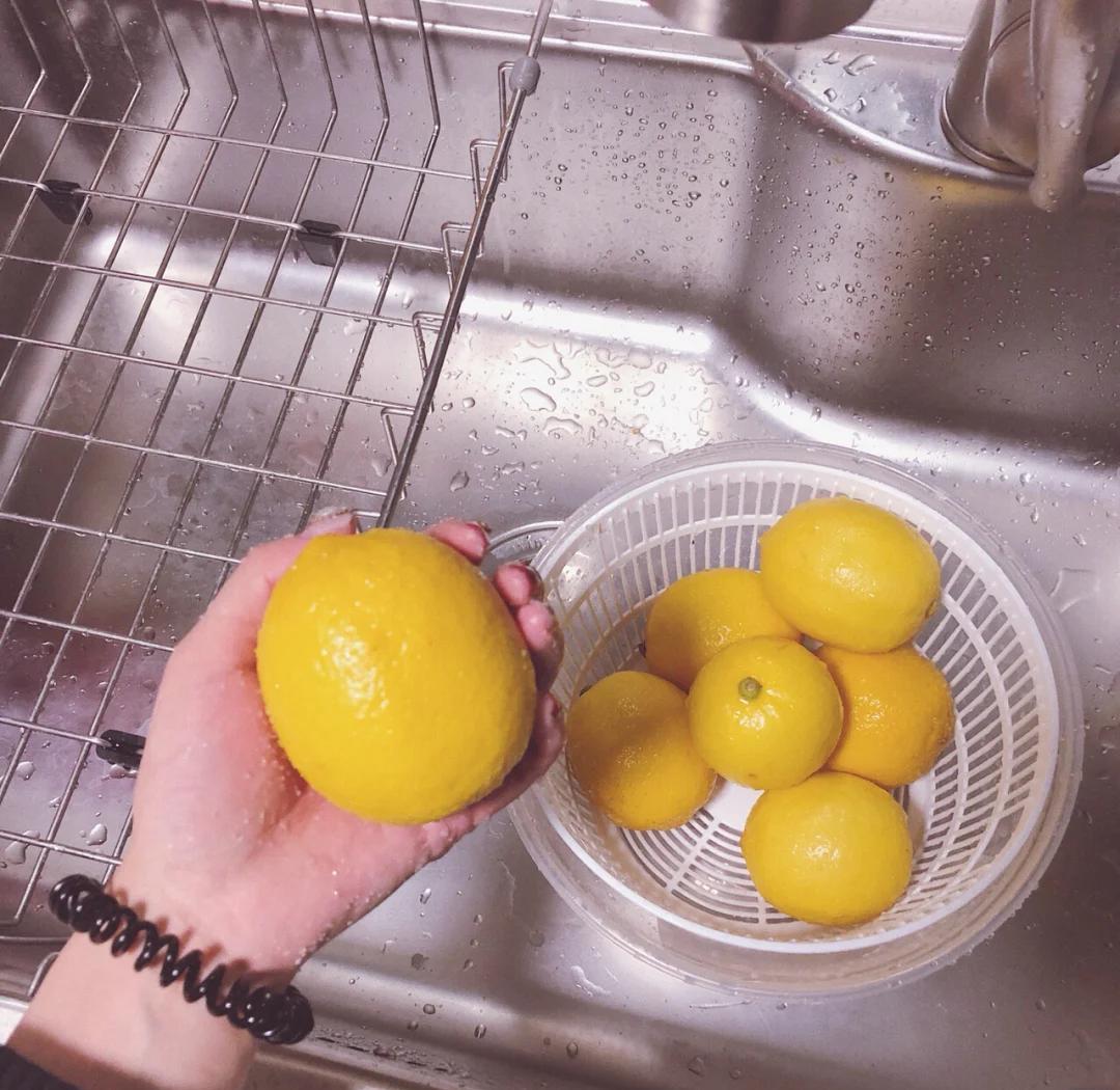 一位女性的手正在用新鲜切开的柠檬片摩擦指尖和手掌,背景为厨房水槽,光线明亮,突出清洁过程 手部特写正在用柠檬片擦拭手指