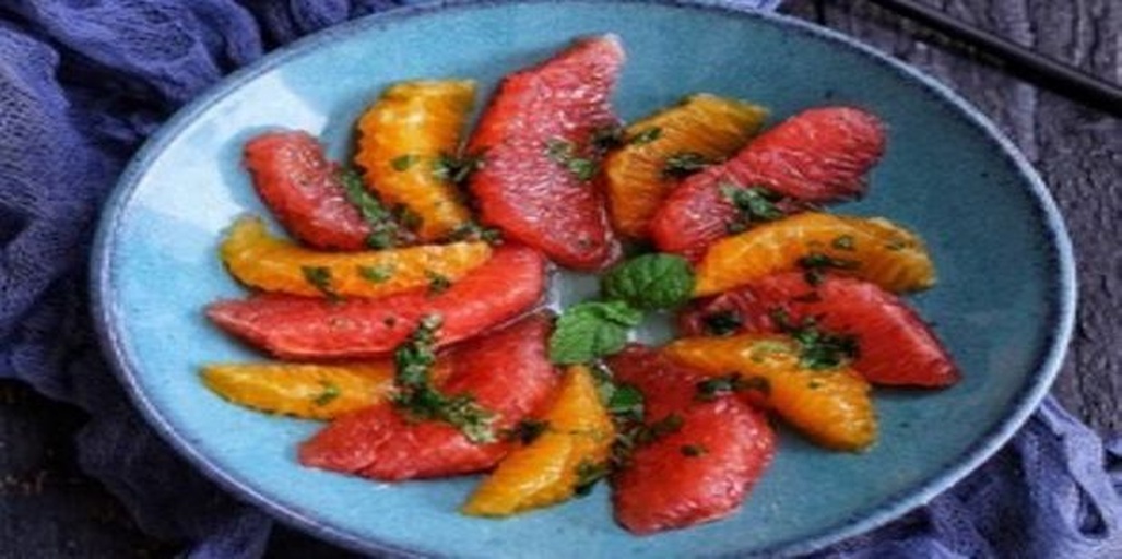 一个由大三红柚果瓣、橙子、蓝莓和猕猴桃组成的圆形果盘,摆放在白色陶瓷盘中,大三红柚位于中心位置,红色果肉格外醒目,周围点缀薄荷叶,整体风格清新自然 大三红柚与其他水果组成的果盘摆拍