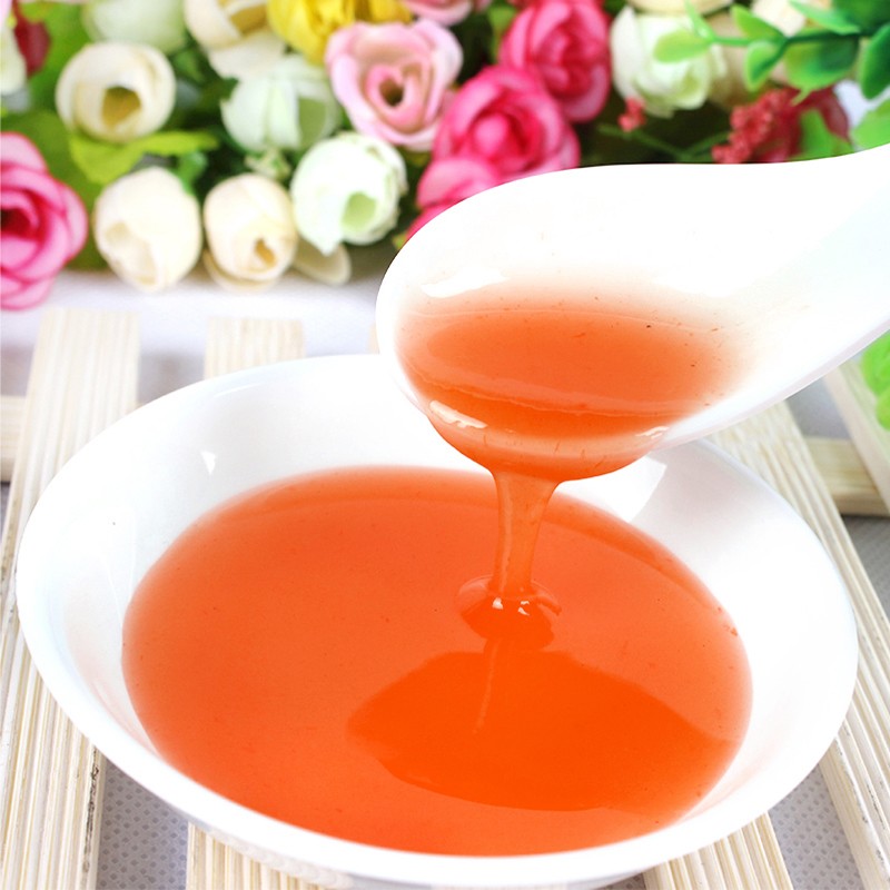 一位厨师正在玻璃碗中将橙色果片与透明糖浆混合，旁边放着茉莉花和蜂蜜罐