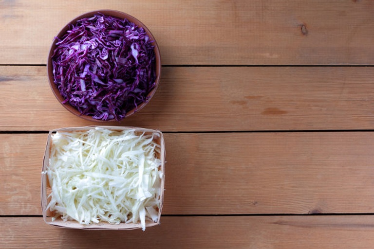 一颗完整的紫色卷心菜置于木质餐桌上,一侧切开展示内部纹理,另一侧是一杯刚榨好的深紫色紫甘蓝汁,旁边配有柠檬片和玻璃搅拌棒,自然光照射下色彩饱满生动 新鲜紫甘蓝与紫甘蓝汁饮品特写