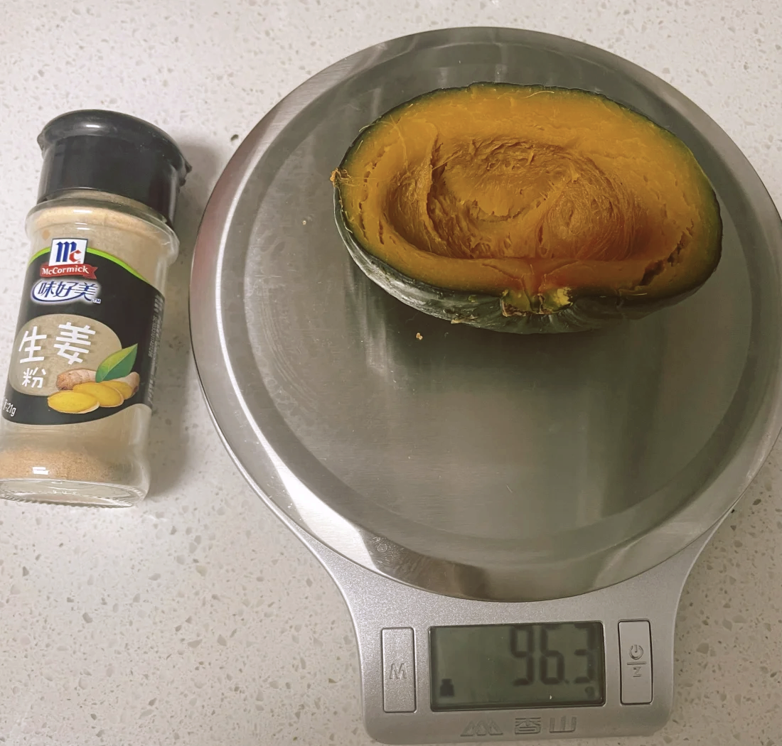 一位年轻女性正在厨房用电子秤称量一段煮熟的白糯玉米,旁边摆放着血糖仪、全麦面包、黄瓜片和一杯牛奶,桌面整洁明亮,体现科学饮食管理场景 图片描述