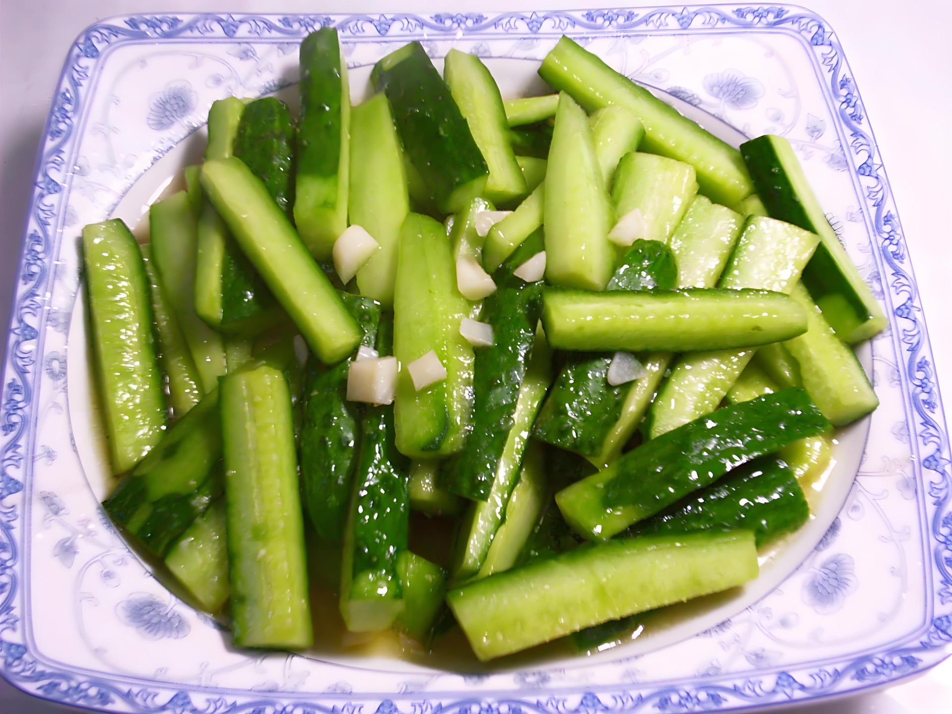 大蒜为主料的凉拌菜品展示其在日常膳食中的应用形式 一盘以大蒜为主要配料的凉拌菜,包含拍碎的大蒜瓣、香菜、红椒丝,置于白色瓷盘中,背景为简约中式餐桌